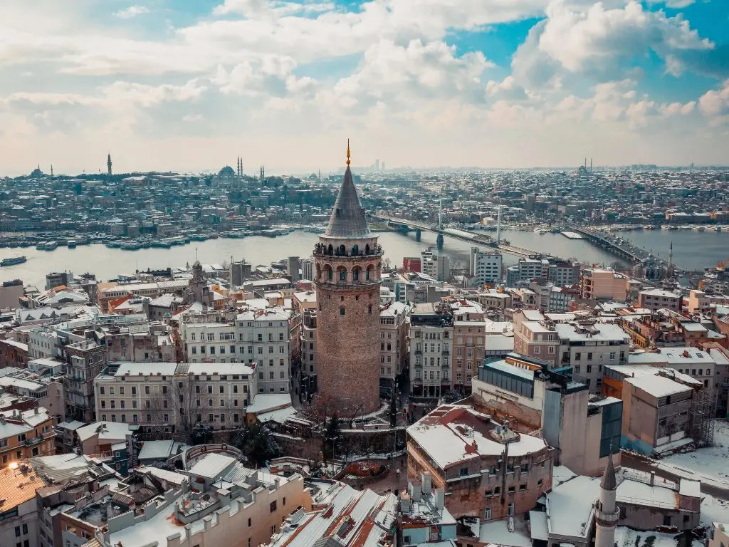 An image showcasing the vibrant skyline of Istanbul, Turkey, featuring the iconic landmark of Galata Tower, illuminated against the bright sky. The cityscape depicts a blend of historical architecture and modern structures, capturing the essence of Istanbul's rich cultural heritage and breathtaking scenery.