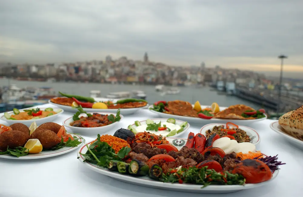 An image showcasing a colorful array of traditional Turkish dishes in Istanbul. Plates filled with delicious kebabs, savory mezes, aromatic Turkish tea, baklava, and various sweets adorn a table, offering a delightful representation of Istanbul's diverse and flavorful culinary heritage. The vibrant presentation highlights the richness of Turkish cuisine, inviting viewers to savor the tastes and aromas unique to this gastronomic culture