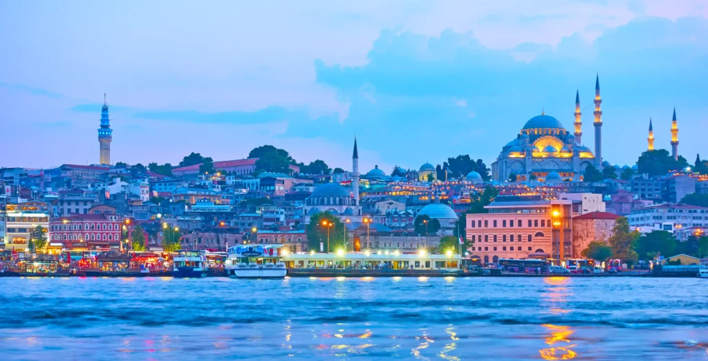 An image capturing the enchanting evening ambiance of Istanbul, Turkey. The cityscape is illuminated by the soft glow of streetlights and the twinkling of buildings along the Bosphorus Strait. The silhouettes of iconic landmarks such as the Blue Mosque and Hagia Sophia stand against the dusky sky, creating a picturesque scene that encapsulates the magical allure of Istanbul's nights.