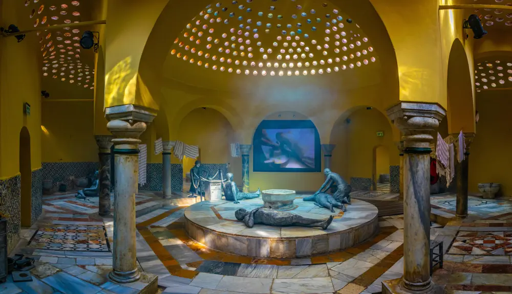 An image portraying the serene ambiance of a traditional Turkish bath, or 'hamam,' in Istanbul. The ornate marble interior features a central heated platform surrounded by basins and arches, evoking a sense of luxury and relaxation. Soft, ambient lighting adds to the tranquil atmosphere, inviting visitors to experience the cultural indulgence and therapeutic rituals of Turkish baths, an integral part of Istanbul's heritage.